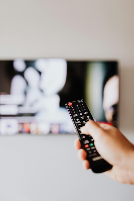 A hand is holding a remote control pointed at a television.