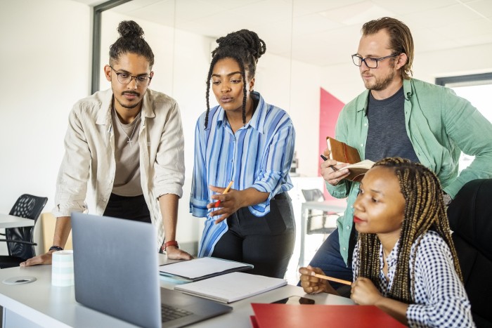 A diverse group of four business people are looking at a laptop while in a meeting together.