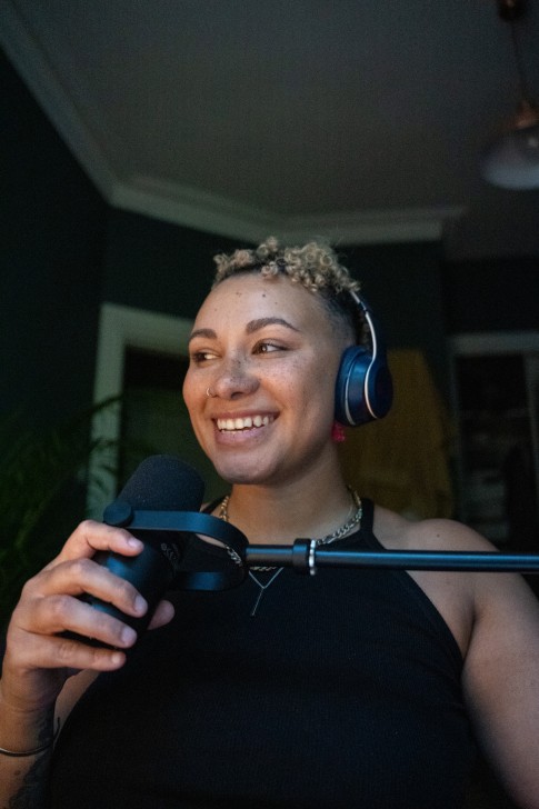 A non-binary person with autism is wearing headphones and using a microphone.