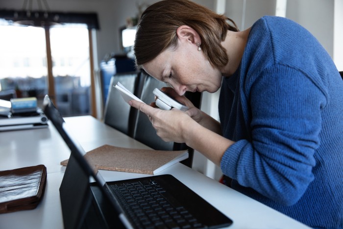 A Blind woman is reading a document through magnifying glass while sitting at home.