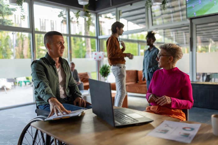 A group of four diverse colleagues are in discussion in a coffee shop with a laptop.