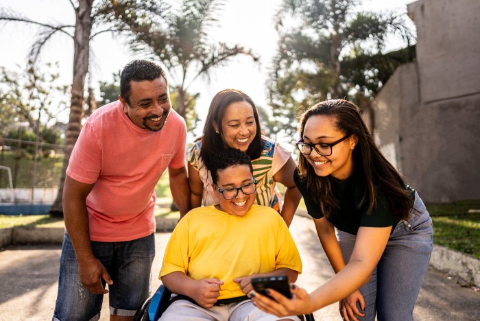 A young man in a wheelchair is with three members of his family in a park using a mobile phone.
