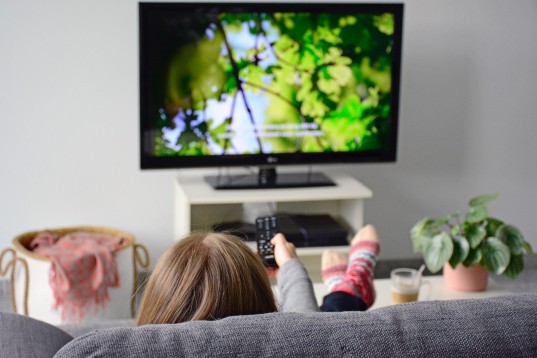 A woman is watching television with subtitles while sitting comfortably on a sofa.