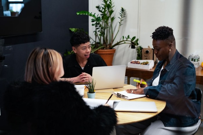 Co-workers of varying genders and ethnicities are sitting around a table for a meeting.